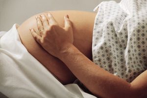 Schwangere liegt im Bett und streichelt ihren Bauch
