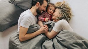 Happy parents cuddling baby son in bed