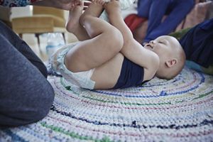 Baby liegt auf dem Rücken; Frau hält die Füßchen in den Händen