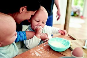 Babys sitzen mit Mutter am Esstisch und essen Brei