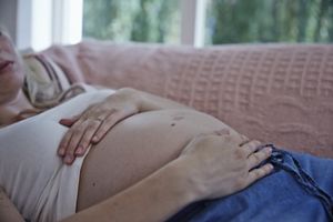 Frau liegt auf Couch und hält den Babybauch