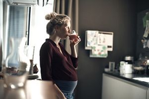 Schwangere Frau trinkt Smoothie in der Küche