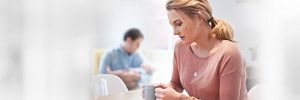 Mutter sitzt am Tisch, Vater im Hintergrund hält Baby im Arm
