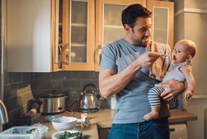 Vater füttern Baby auf seinem Arm einen Löffel Brei