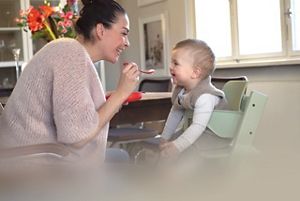Mama füttert glückliches Baby im Hochstuhl