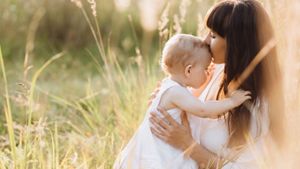 Beautiful portrait of charming mother and lovely little daughter walking across the field in the rays of evening sun