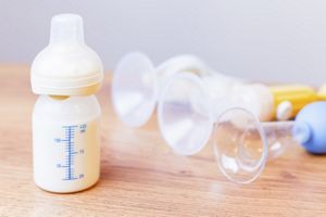 Baby bottle with milk and manual breast pump at background