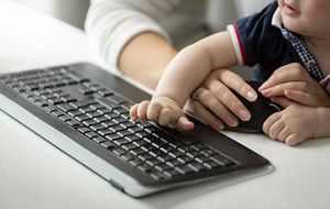 Cute baby boy sitting on mothers lap while she is working at computer